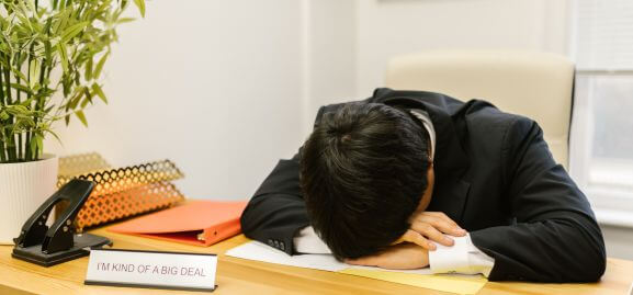 A man puts his head on the desk out of tiredness, another reason why escaping the rat race is a must.